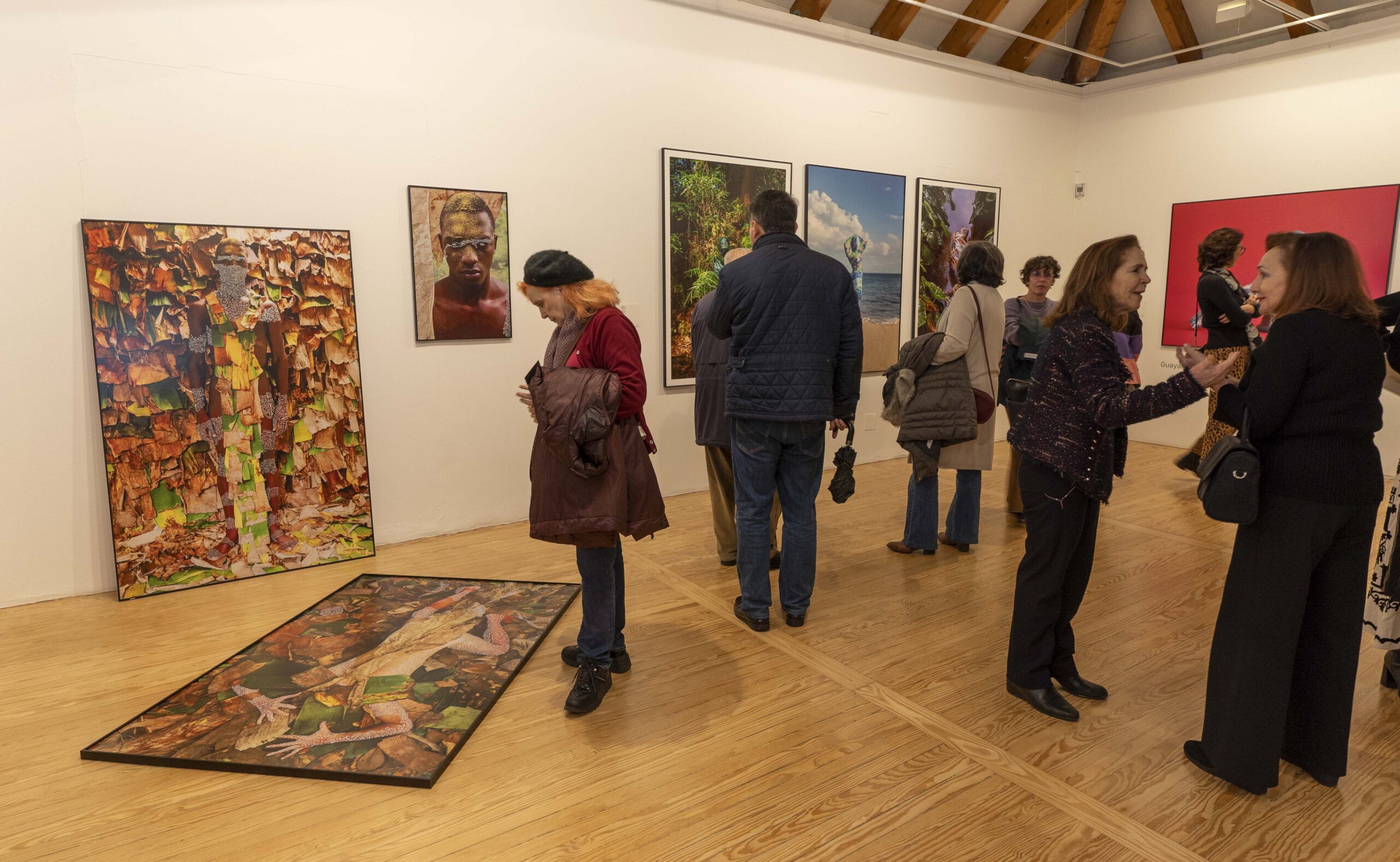 Una sala de exposición de arte en ARCO Madrid llena de personas observando diversas obras de arte en las paredes. La gente conversa y admira las impresiones artísticas y fotográficas.