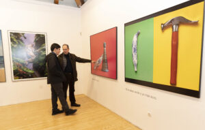 Una sala de exposición de arte en ARCO Madrid dos personas observando diversas obras de arte en las paredes. La gente conversa y admira las impresiones artísticas y fotográficas.